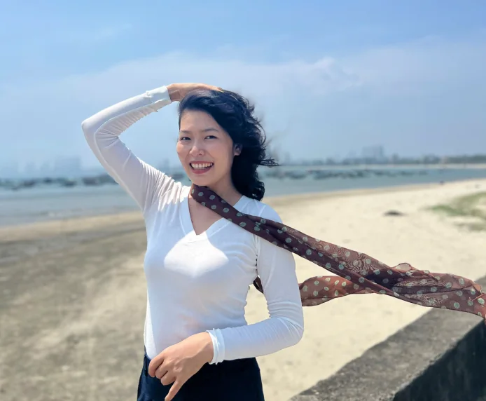 Lanah laughing on a beach with a brown scarf blowing in the wind